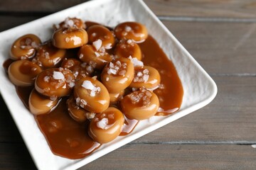 Plate with tasty candies, caramel sauce and salt on wooden table
