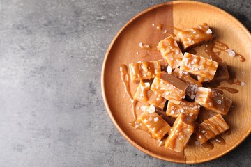Plate with tasty candies, caramel sauce and salt on grey table, top view. Space for text