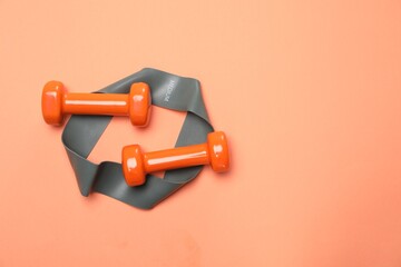 Dumbbells and fitness elastic band on coral background, flat lay. Space for text