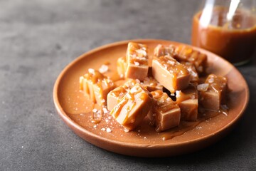 Plate with tasty candies, caramel sauce and salt on grey table, closeup