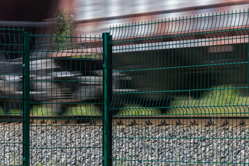 A metal fence behind which a train passes. Railroad fencing. Ensuring the safety of railway...