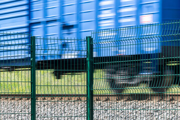 Obraz premium A metal fence behind which a train passes. Railroad fencing. Ensuring the safety of railway transport. Steel fence