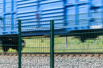 Obraz premium A metal fence behind which a train passes. Railroad fencing. Ensuring the safety of railway transport. Steel fence