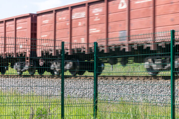 A metal fence behind which a train passes. Railroad fencing. Ensuring the safety of railway...