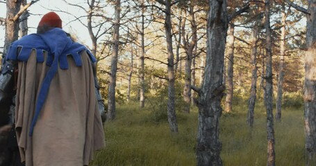 Walking in the forest A man with a beard in a medieval costume of a knight looking around. Back view. Close-up. Reconstruction of historical events