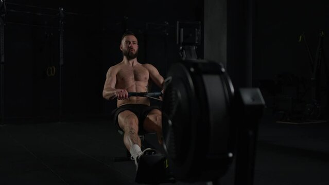 Man exercising on rowing machine, wearing only shorts, bare chest. Routine workout for physical and mental health.