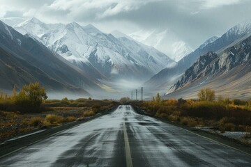 Fototapeta premium Wet, deserted road leading towards snowcapped mountains with dramatic clouds