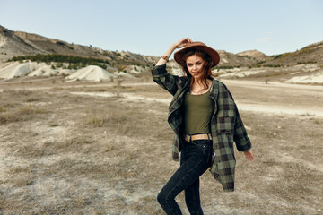 Confident woman in plaid jacket and hat standing in desert with hands on hips