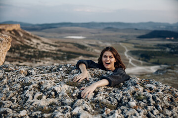 Woman sitting on rock, hands on face, mouth open in shock and disbelief against scenic landscape