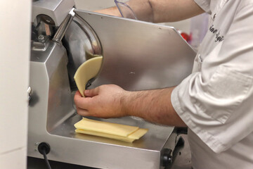 Unrecognizable person cutting cheese with a machine in a restaurant kitchen, dressed in uniform, to make meals