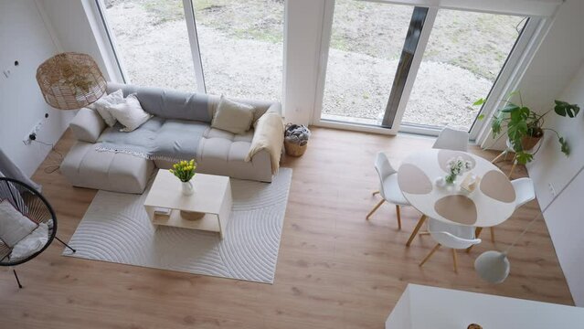 Living room interior with sofa, wooden coffee table with simple decorations, carpet on hardwood floor. Big panoramic window.