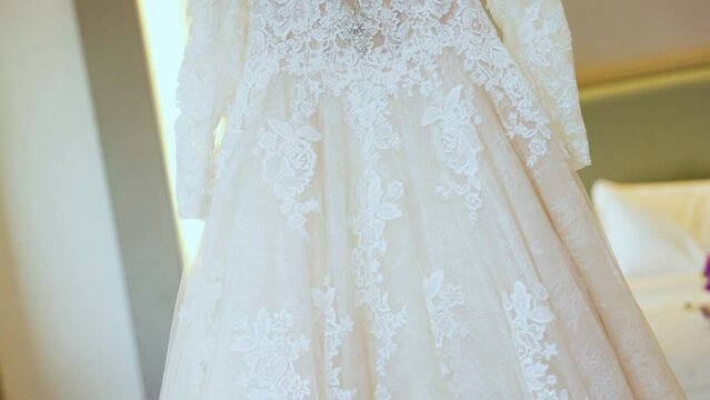 White wedding gown hangs on a wooden hanger from the celling 60fps