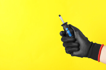 Woman holding small screwdriver on yellow background, closeup. Space for text