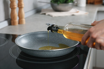 Vegetable fats. Woman pouring cooking oil into frying pan on stove in kitchen, closeup