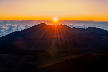 Sunrise shine on the top of Haleakala volcano mountain with sunbeams shine over clouds sky...