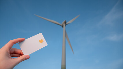 A person is holding a credit card next to a wind turbine