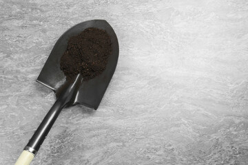 Metal shovel with fertile soil on grey textured surface, top view. Space for text