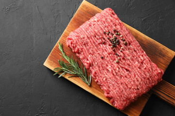 Raw ground meat, rosemary and peppercorns on black table, top view. Space for text