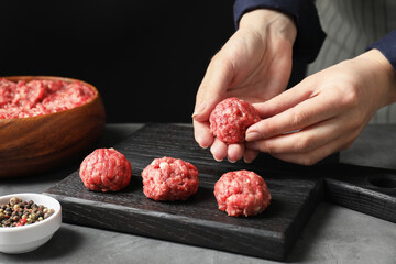 Woman making meatball from ground meat at grey table, closeup