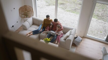 Top view of family with small daughter sitting on sofa in their new home. Young family buying a first house, big milestone and home ownership concept.