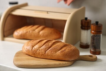 Wooden bread basket with freshly baked loaves on white marble table in kitchen