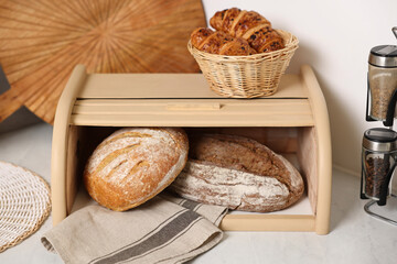 Wooden bread basket, freshly baked loaves and croissants on white marble table in kitchen