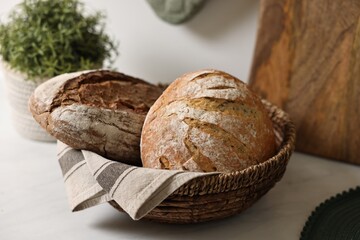Wicker bread basket with freshly baked loaves on white marble table in kitchen