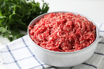 Raw ground meat in bowl and parsley on table, closeup