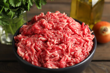 Raw ground meat in bowl and parsley on wooden table, closeup