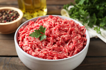 Raw ground meat in bowl, parsley, spices and oil on wooden table, closeup