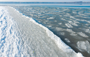 Ice floating near the shore in the form of oblong ice floes, rolled around by waves and a storm in the Tiligul estuary