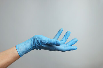 Doctor wearing light blue medical glove holding something on grey background, closeup