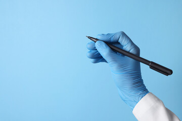 Doctor wearing medical glove writing something on light blue background, closeup. Space for text