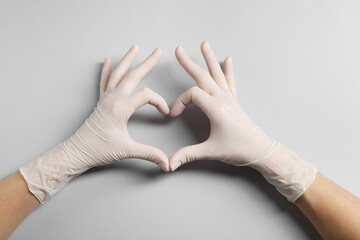 Doctor wearing white medical gloves making heart gesture on grey background, top view