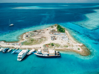 Dump island and yacht harbor in Maldives. Aerial view of pollution by plastic rubbish dump