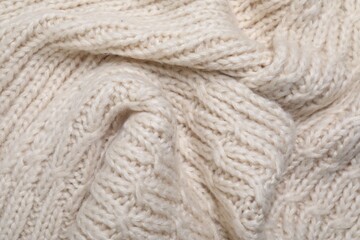 Beige knitted scarf as background, top view