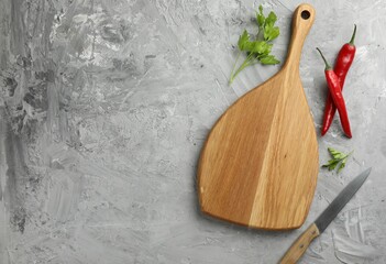 Cutting board, knife, chili peppers and parsley on grey textured table, flat lay. Space for text