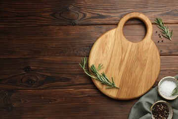 Cutting board, salt, pepper and rosemary on wooden table, flat lay. Space for text