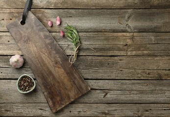 Cutting board, garlic, pepper and rosemary on wooden table, flat lay. Space for text