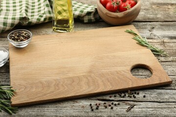 Cutting board, rosemary, oil and pepper on wooden table. Space for text