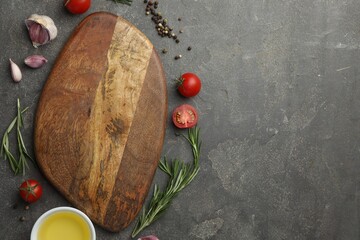 Cutting board, rosemary, garlic, oil and tomatoes on black table, flat lay. Space for text