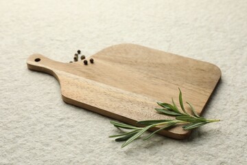 Cutting board, pepper and rosemary on white textured table. Space for text