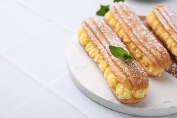 Delicious eclairs filled with cream and mint on white tiled table, space for text