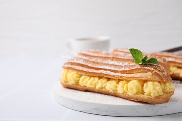 Delicious eclairs filled with cream and mint on white table, closeup. Space for text