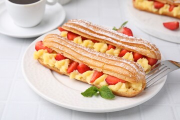 Delicious eclairs filled with cream, strawberries and mint on white tiled table