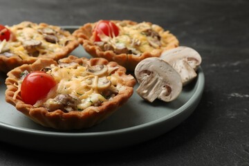 Tasty tartlets with cheese, mushrooms and tomatoes on dark table, closeup