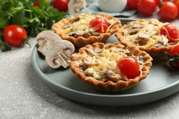 Tasty tartlets with cheese, mushrooms and tomatoes on grey table, closeup