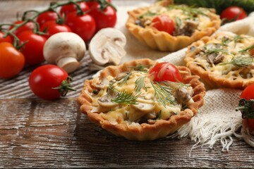 Tasty tartlets with cheese, tomatoes, mushrooms and dill on wooden rustic table, closeup