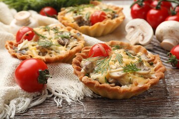 Tasty tartlets with cheese, tomatoes, mushrooms and dill on wooden rustic table, closeup