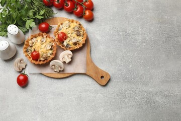 Tasty tartlets with cheese, mushrooms and tomatoes on grey table, flat lay. Space for text